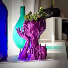 a purple vase with plants in it next to a blue bottle