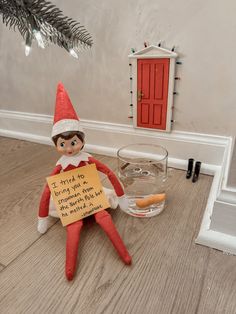 an elf with a sign sitting on the floor next to a glass of water and a hot dog