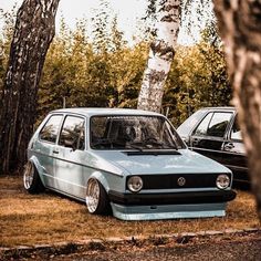 two cars parked next to each other in front of some trees and grass on the ground