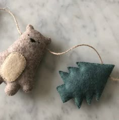 two felt ornaments on a marble surface one has a bear and the other is a tree