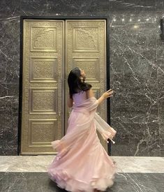 a woman in a long pink dress is standing by a door and looking up at the sky