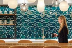 a woman standing in front of a counter with lots of chairs and lights hanging from the ceiling