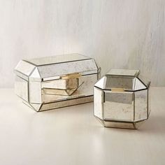 two mirrored boxes sitting next to each other on top of a wooden table with a white wall in the background