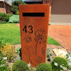 a metal mailbox sitting in the middle of some flowers and grass next to a house