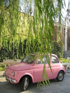 an old pink car is parked under a tree