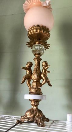 an antique lamp with two cherubs on the base and a pink glass shade