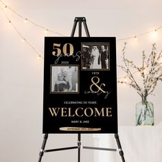 a black and gold 50th anniversary welcome sign on a easel with lights in the background