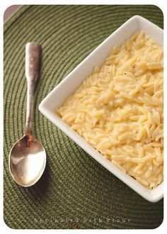 a bowl of macaroni and cheese next to a spoon on a green place mat