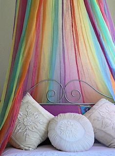 a canopy bed with four pillows on top of it and multicolored net hanging from the ceiling