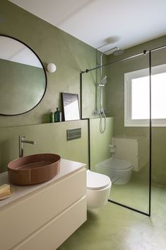 a bathroom with green walls and a round mirror above the toilet, along with a brown bowl sink