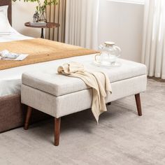 a bed with a white blanket on top of it next to a table and chair