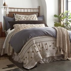 a bed with two pillows and blankets on top of it next to a potted plant