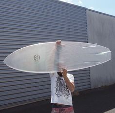 a man holding up a surfboard in front of a metal building on the street