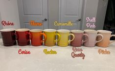 six different colored coffee mugs lined up on a counter