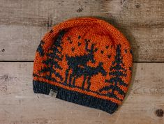 an orange and black knitted beanie with trees on it sitting on a wooden surface