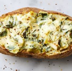 a baked potato with cheese and spinach on the top is sitting on a white surface