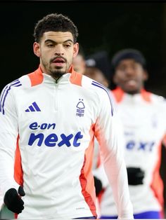 the soccer player is wearing an orange and white uniform while standing in front of other players