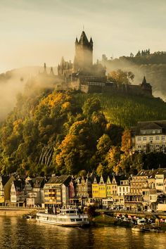 a castle on top of a hill next to a river with boats in the water