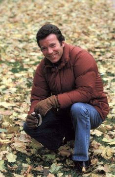 a man kneeling down in the leaves with a glove on his hand and smiling at the camera