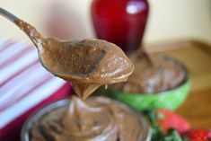 a spoon full of chocolate frosting with strawberries in the background