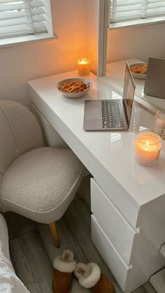 a laptop computer sitting on top of a white desk next to a candle and a bowl of food