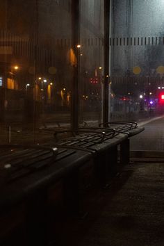 a bench sitting in front of a window on a street at night with traffic lights