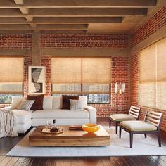 a living room with brick walls and wooden floors, white couches and chairs in front of the windows