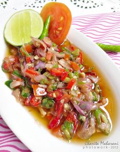 a white plate topped with lots of food next to a slice of lime and tomato