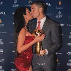 a man and woman kissing each other while holding an award