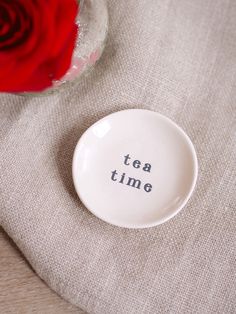 a white plate with the words tea time written on it next to a red rose