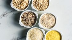 six bowls filled with different types of cereals and grains on a marble counter top