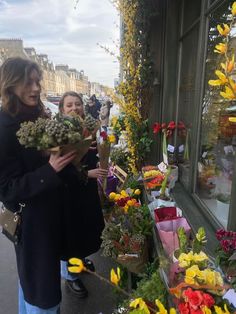 two women are looking at flowers in front of a flower shop