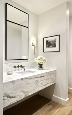 a white bathroom with marble counter tops and double sinks, framed pictures on the wall