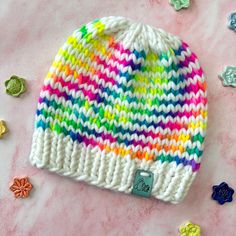 a multicolored knitted hat sitting on top of a pink table next to buttons