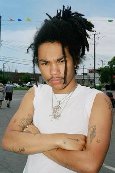 a man with dreadlocks standing in the middle of a parking lot wearing a white t - shirt