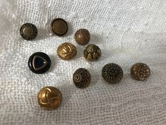 several different types of buttons laying on a white cloth with some gold and black ones