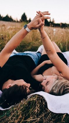 a man and woman laying on top of a blanket in the middle of a field