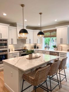 a large kitchen with white cabinets and marble counter tops, two pendant lights over the island