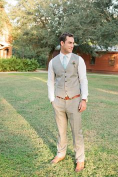 a man standing in the grass wearing a suit and tie with his hands in his pockets