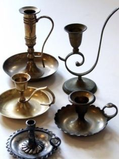 an assortment of metal items on a white table top, including candlesticks and saucers