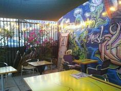 tables and chairs are in front of a colorful wall with graffiti on it, along with potted plants