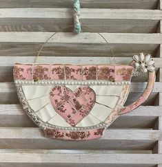 a pink and white teapot hanging on a wooden wall with two hearts in it