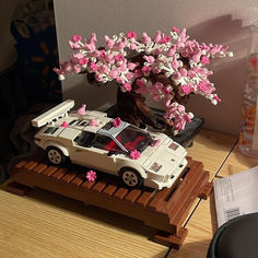 a toy car with pink flowers on the roof is parked under a tree in front of an open book