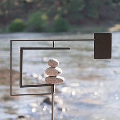 a sculpture made out of rocks sitting on top of a metal stand next to a river