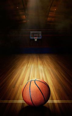 a basketball sitting on top of a wooden floor in front of a basket ball at night