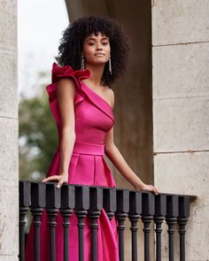 a woman in a pink dress leaning on a balcony rail with her hand on the railing