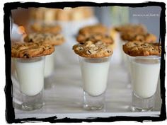 there are cookies and milk in small cups on the table with other food items behind them