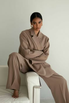 a woman sitting on top of a white couch wearing a tan coat and matching pants