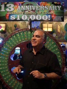 a man is standing in front of a wheel of cash sign with balloons around him