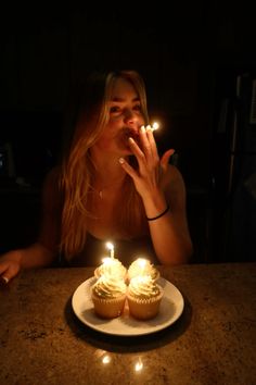 a woman sitting at a table with two cupcakes in front of her face